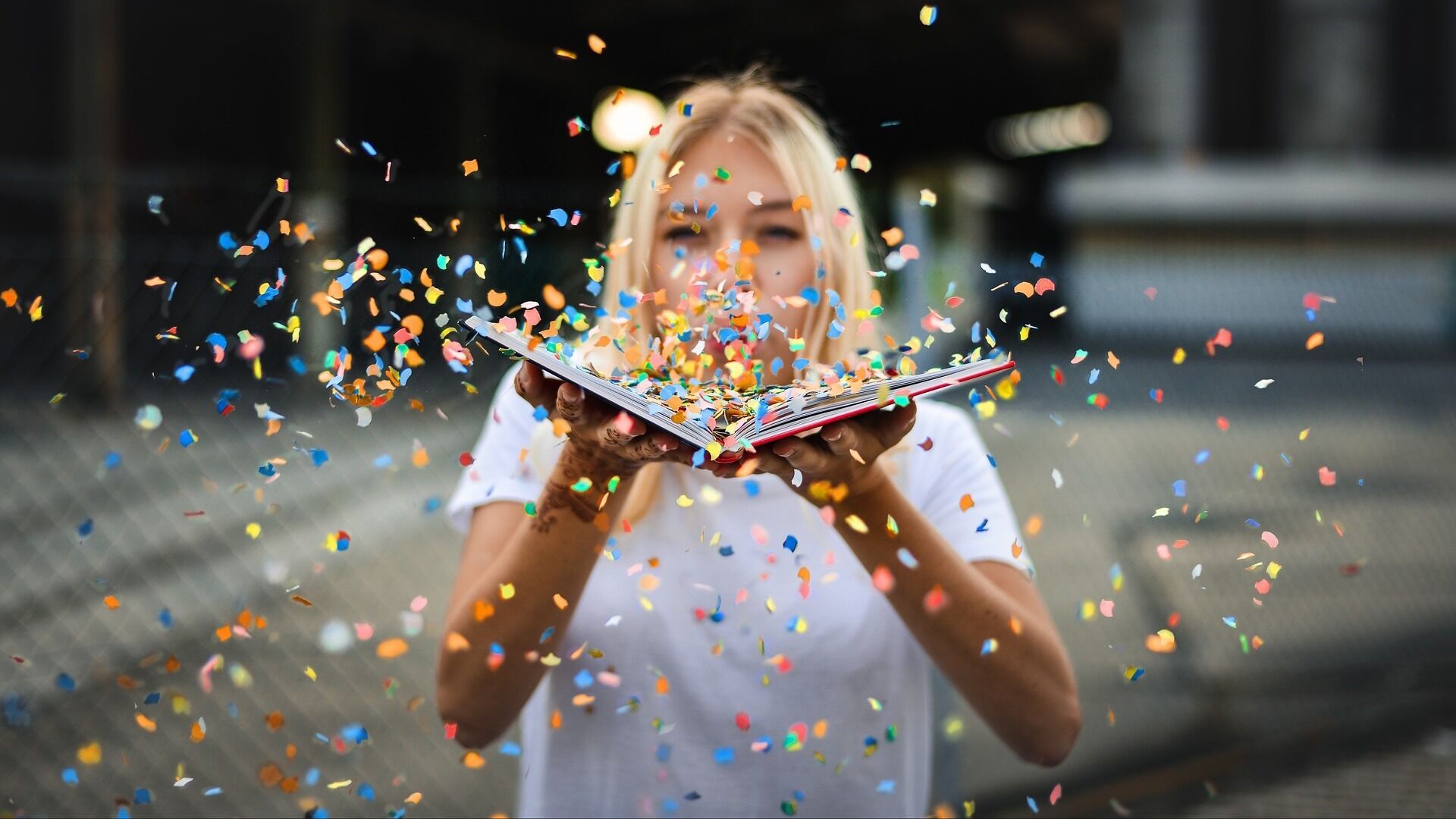 A person is holding a book open and blowing confetti from the pages.