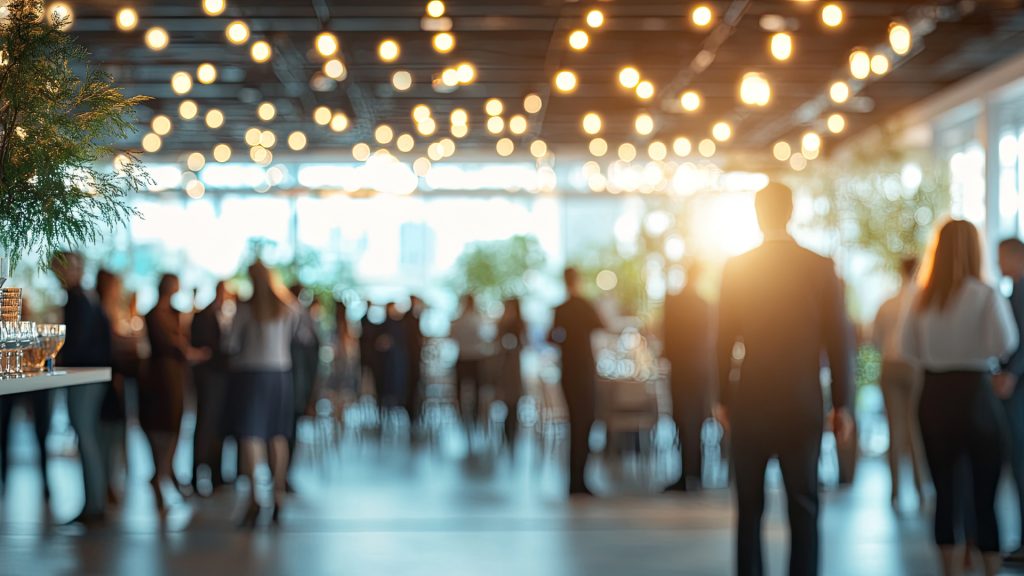 Blurred image of people mingling at a social event under warm lights.