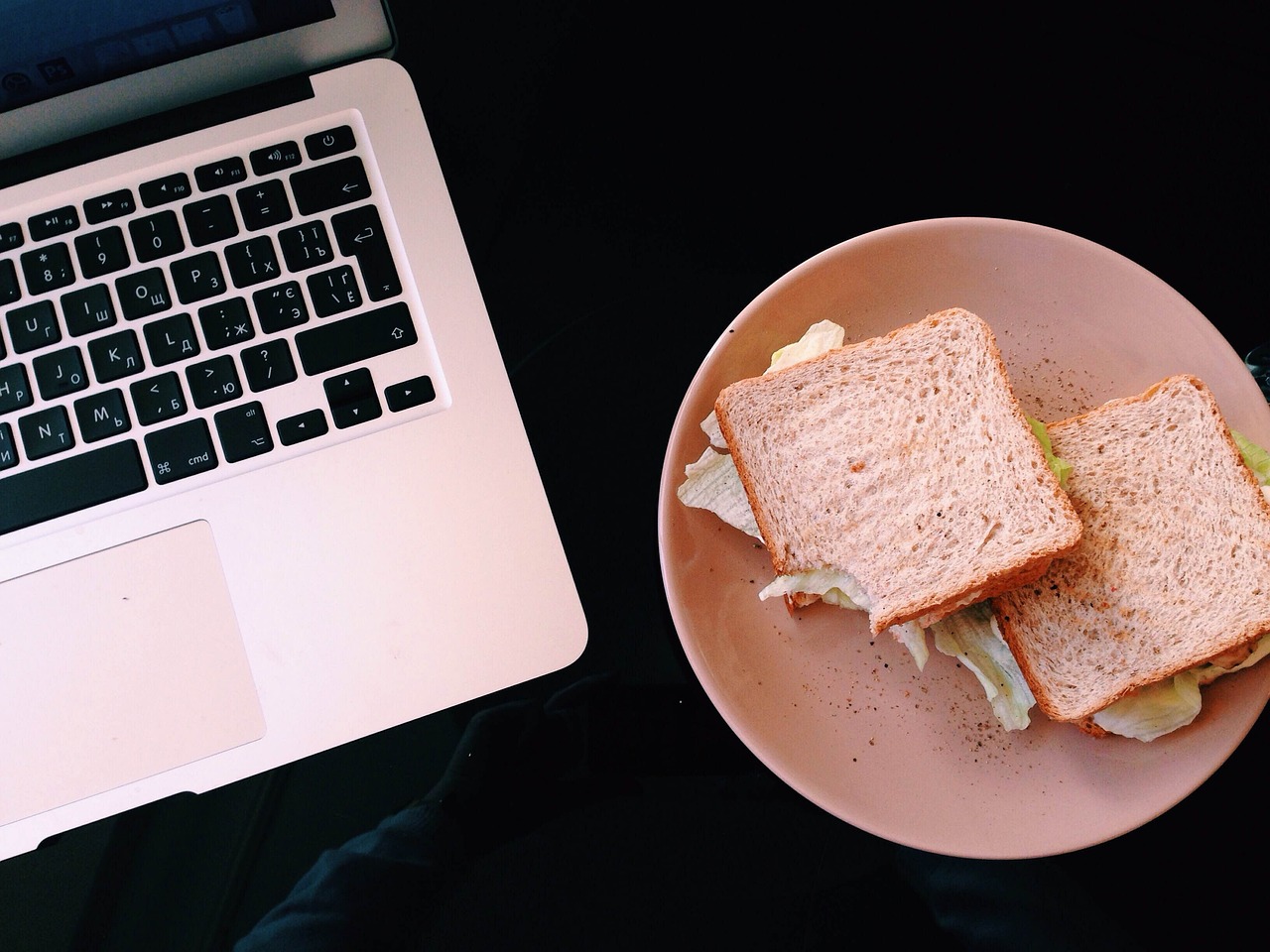 A laptop next to a plate with two homemade sandwiches.