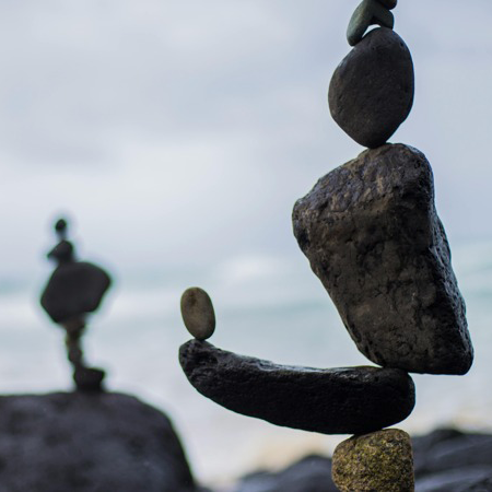 Photo of stones balanced in a stack on top of large boulders on the beach.